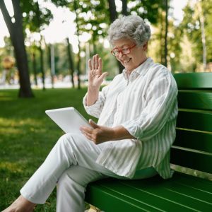An elderly woman in glasses using laptop on bench An elderly woman in glasses using laptop on bench