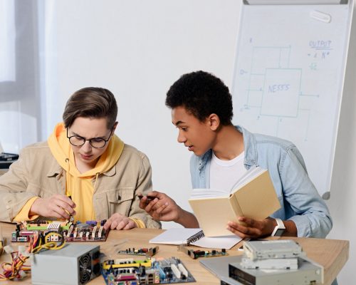 multicultural teen boys studying and repairing computer motherboard at home